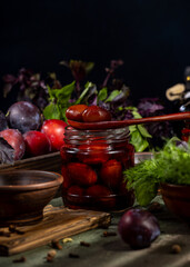 Pickled plums in jar with wooden spoon and fresh herbs