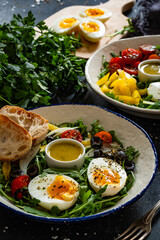 Fresh green salad with vegetables, boiled eggs and vinaigrette sauce on black table