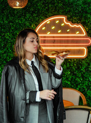 Joven empresaria comiendo pizza frente a luces de neón en la calle