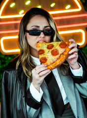 Joven empresaria comiendo pizza frente a luces de neón en la calle