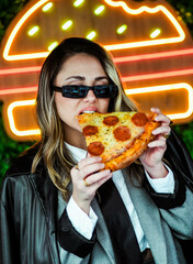 Joven empresaria comiendo pizza frente a luces de neón en la calle