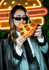 Joven empresaria comiendo pizza frente a luces de neón en la calle