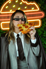 Joven empresaria comiendo pizza frente a luces de neón en la calle