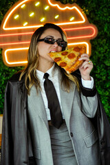 Joven empresaria comiendo pizza frente a luces de neón en la calle