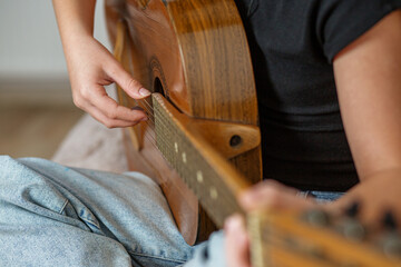 Child enjoying practice session while playing acoustic guitar at home in afternoon. Close up