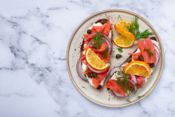 sandwich with freshly smoked salmon, on black bread, with cottage cheese, with herbs and red onions, capers and pieces of citrus fruits, on a marble countertop, breakfast, no people,