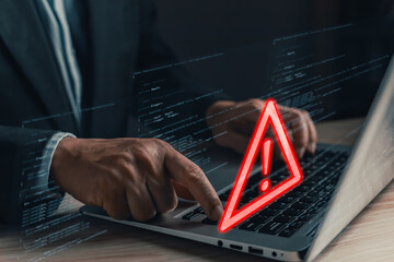 A professional uses a laptop displaying a glowing red warning triangle with an exclamation mark,...