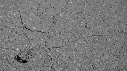 Obraz premium Top down view of cracked asphalt with pebbles featuring stylish sunglasses in bottom left corner