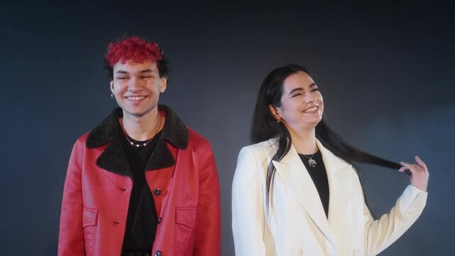 A young guy in a red jacket stands with a young girl in a white jacket on a dark background. The guy makes excuses, the girl rejoices.