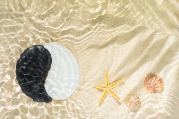 sun lights with hard shadow of palm leaf in wavy water on abstract sand background with shell, starfish and sign Yin-Yang stones, beautiful abstract spa concept