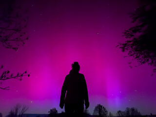 Silhouette of woman admiring vibrant pink aurora borealis in La Cerdanya, Pyrenees, Spain. May 2024