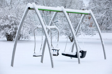 Lonely and empty snow-covered children's swings in the park on a winter day