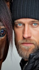 Close-up of a man with striking blue eyes alongside a horse, emphasizing their connection and intensity in a soft-lit setting