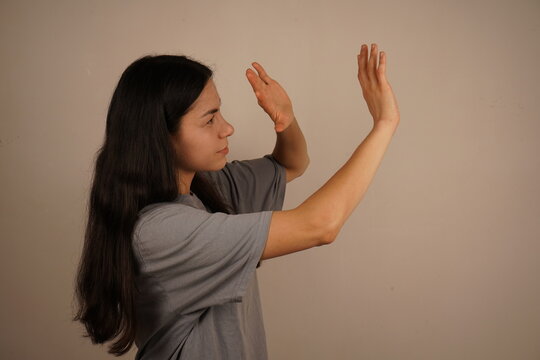 The gesture symbolizes the instinctive response to danger. It highlights the theme of domestic violence. A woman holds both hands in front of her face, a defensive posture expressing fear and