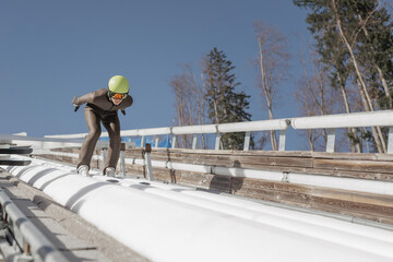 Fototapeta premium Ski jumper sitting on a start bar on top of ski jump focusing on speeding up down the inrun track. Winter sports concept.