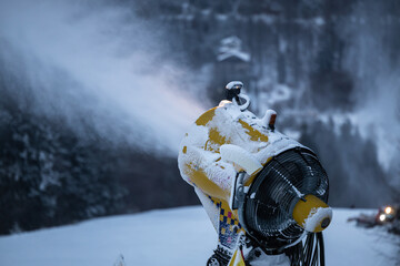 Snow cannon in the evening. Snow making machine on ski slope in the evening to prepare the mountain ski resort for the next day. Winter sports industry.