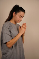 Fototapeta premium The dark-haired woman folds her hands in prayer, palms meeting in a heartfelt gesture. Her closed eyes and calm demeanor symbolize spiritual connection. A serene image of sincerity and hope.