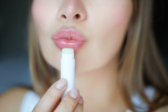 Close-up of a woman applying hydration hygienic lip balm, showcasing glossy pink pout lips and natural beauty skin care treatment