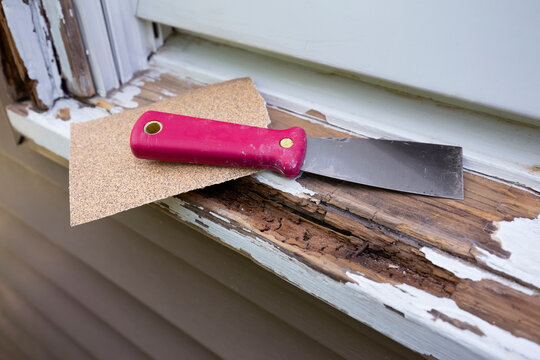 Repairing rotten wood window sill with a putty knife and sandpaper