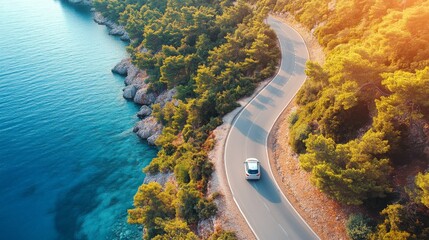 A compact urban car drives along a winding coastal road surrounded by lush greenery and a clear blue sea