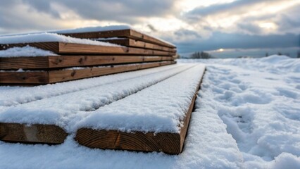Medium closeup image highlighting a pile of wooden boards covered in a thick layer of fluffy snow with traces of footprints leading to the materials suggesting recent use.