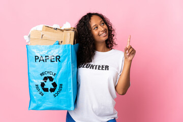 Teenager cuban girl holding a recycling bag full of paper to recycle isolated on pink background...