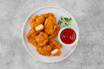 Crispy chicken nuggets with ketchup on a white plate on a gray concrete background.