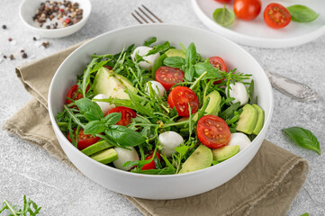 Fresh salad with arugula, mozzarella, tomatoes and avocado in a bowl. Healthy vegetarian dish.
