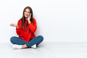 Young Ukrainian woman sitting on the floor isolated on white background keeping a conversation with the mobile phone with someone