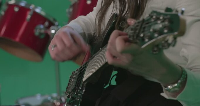 Close-up shot of a woman's hands playing an electric guitar. The focus is on her finger movements as she strums the strings against a green screen background. 