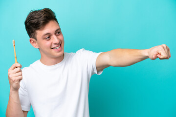 Young Brazilian man brushing teeth isolated on blue background giving a thumbs up gesture