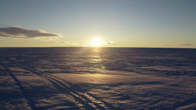 Sunset in Antarctica. Endless snow landscape. Earth ecology protection. Global warming and ice melting. Drone camera flies to the sun direction.