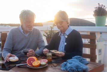 Smiling caucasian retired elderly couple enjoying a healthy breakfast together on the home terrace.
