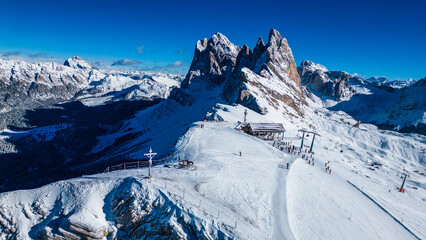 Seceda on the Val Gardena resort presents an awe-inspiring winter spectacle, captured from the air by drone. Its iconic jagged peaks rise dramatically above snow-covered slopes