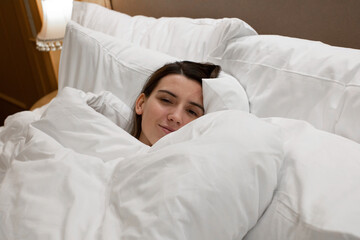 young woman waked up in cozy bed with soft pillows