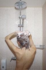 young woman washing hair with shampoo foam in shower, vertical photo