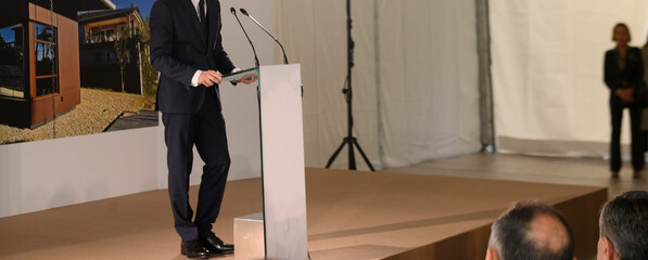 unrecognizable businessman in blue suit speaks into microphones at event
