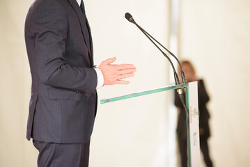 unrecognizable businessman in blue suit speaks into microphones at event