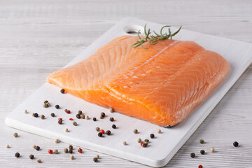 Fresh salmon fillet on a cutting board with colorful peppercorns and herbs for meal preparation