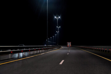 The night highway curves, street lights are on, a moving truck is visible. Background. Landscape.