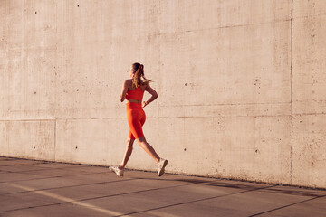 Rear view of fit woman running outdoors against concrete wall