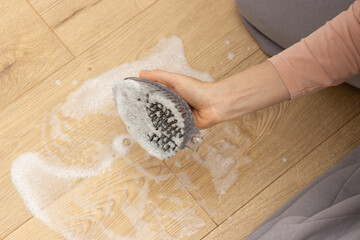 Close-up of a person scrubbing a soapy wooden floor with a hand brush.  household cleaning and hygiene efforts. home cleaning and maintenance 