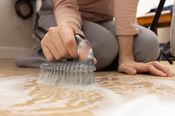 Close-up of a person scrubbing a soapy wooden floor with a hand brush.  household cleaning and hygiene efforts. home cleaning and maintenance 