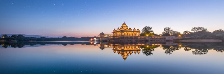 Fototapeta premium Illuminated temple reflected in calm lake at dawn.