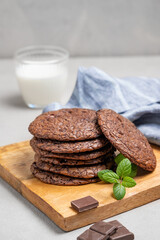 Stack of chocolate cookies on a wooden board on a light background with a glass of milk and napkin.