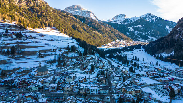 Campitello di Fassa in winter transforms into a magical alpine retreat, nestled in the heart of the Dolomites. Snow-covered peaks, charming village architecture captured by drone