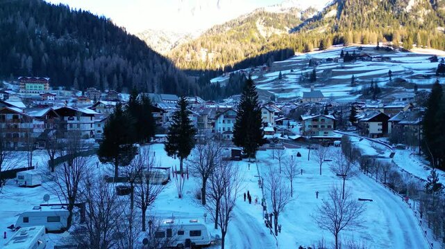 Campitello di Fassa in winter transforms into a magical alpine retreat, nestled in the heart of the Dolomites. Snow-covered peaks, charming village architecture captured by drone