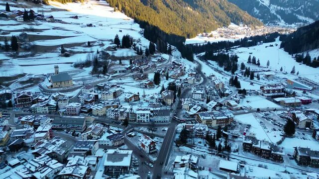Campitello di Fassa in winter transforms into a magical alpine retreat, nestled in the heart of the Dolomites. Snow-covered peaks, charming village architecture captured by drone