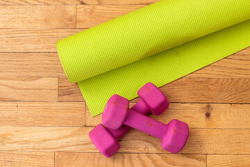Fitness equipment: yoga mat and dumbbells on hardwood floor.