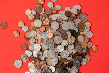 Pile of various coins scattered on a red background.